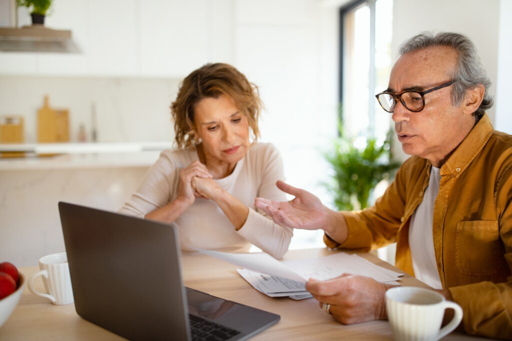 Confused Senior Husband And Wife Checking Their Monthly Expenses Reading Bills Sitting In Front Of